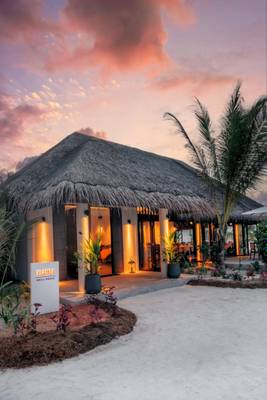 Außenansicht der Nova Maldives Grill House bei Sonnenuntergang mit beleuchteten Eingängen.