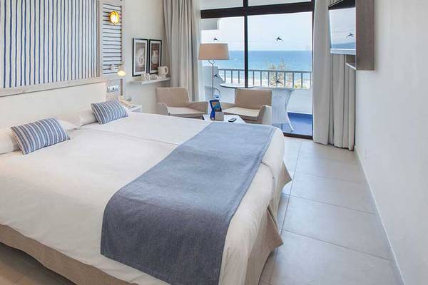 Doppelzimmer mit Meerblick im Corallium Beach Hotel, mit zwei Betten, blauen Kissen und einer Aussicht auf das Meer.