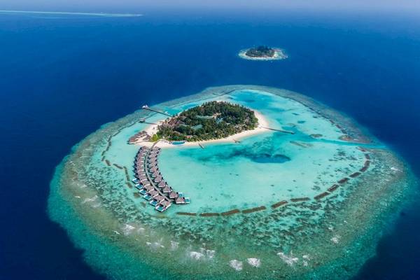 Luftaufnahme des Nova Maldives Resorts, zeigt die Insel mit Wasservillen und blauem Meer.