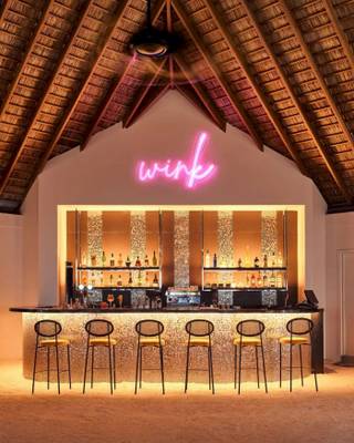 Bar im Nova Maldives Hotel mit leuchtendem Wink-Schild und gefüllten Regalen