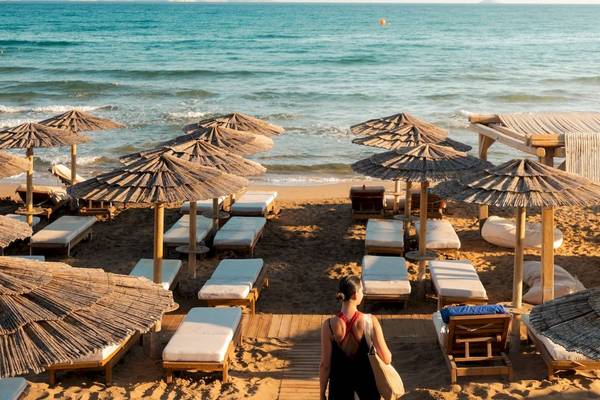 Eine Frau auf dem Strand des Mitsis Selection Rinela Hotels, umgeben von Liegen und Sonnenschirmen.