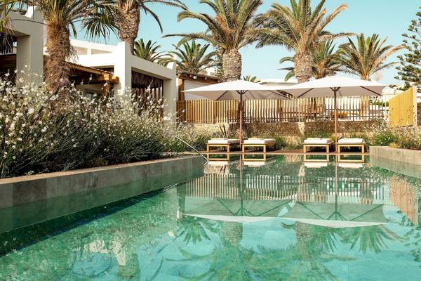 Pool im Mitsis Selection Rinela Hotel mit weißen Sonnenschirmen und Liegen.