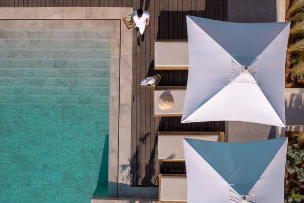 Mitsis Selection Rinela Hotel Außenbereich mit Pool, Sonnenliegen und Sonnenschirmen.