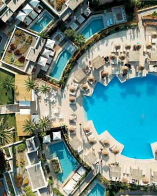 Luftaufnahme des Mitsis Selection Rinela Hotel Pools mit Liegestühlen und Sonnenschirmen.