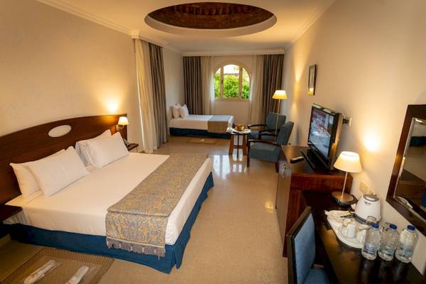 Innenansicht eines Hotelzimmers des Stella Gardens Resort mit Doppelbett, Beibett, Fernseher und Schreibtisch