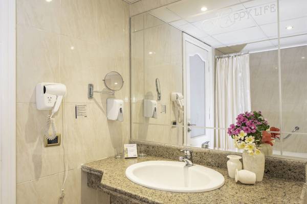 Badezimmer im Three Corners Happy Life Beach Resort mit Spiegel, Waschbecken und Blumenvase.