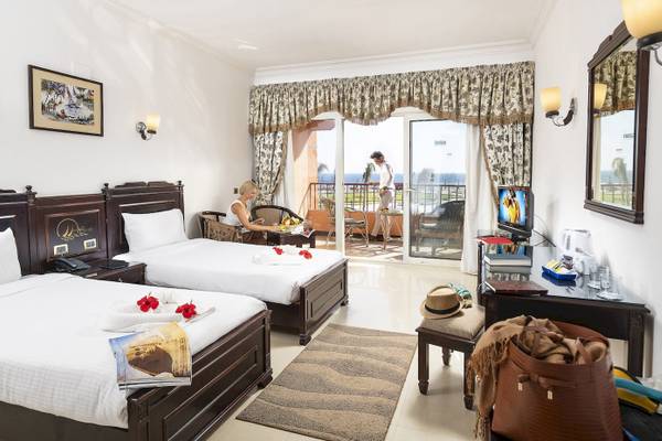 Zimmer im Three Corners Happy Life Beach Resort mit zwei Betten, einem Fernseher, einem Schreibtisch und einer Aussicht auf das Meer.