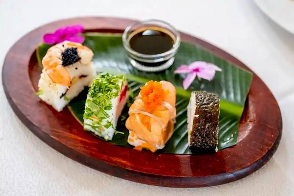 Ein Teller mit verschiedenen Sushi-Variationen auf einem Blatt serviert, mit Sojasauce.