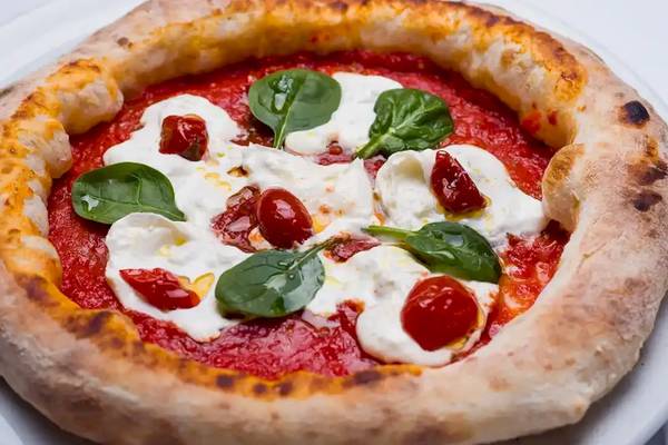Pizza mit Mozzarella und Spinat auf einem weißen Teller serviert