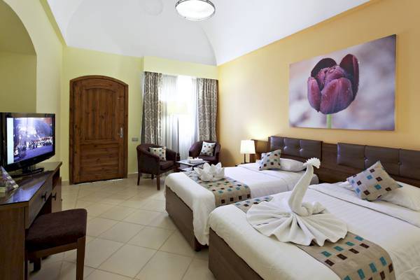 Innenansicht eines Doppelzimmers im Three Corners Rihana Resort mit zwei Betten, Fernseher, Dekor und Möbeln.