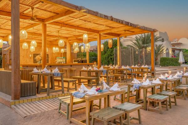 Strandrestaurant des Three Corners Rihana Resorts mit Holztischen und Stühlen, unter einem Strohdach mit Kerzen und Laternen.