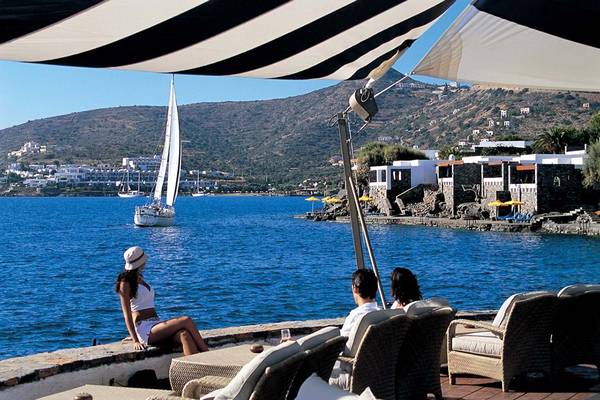 Außenterrasse des Elounda Beach Hotel mit Blick auf das Meer und ein Segelboot.