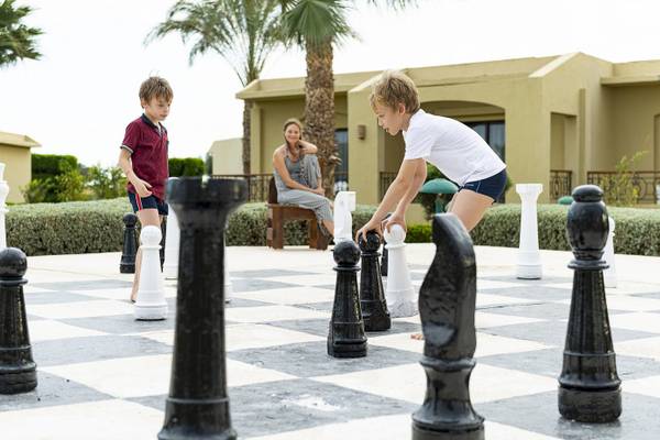 Zwei Kinder spielen Schach im Freien neben einem Hotel.