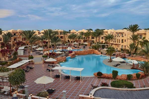 Außenbereich des Steigenberger Coraya Beach Hotels mit Swimmingpool, Liegestühlen und Palmen.