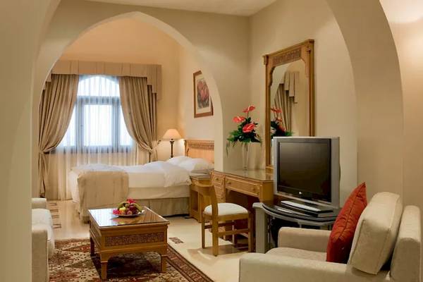 Innenansicht eines luxuriösen Zimmers im Mövenpick Resort Sharm el Sheikh mit einem Doppelbett, Fernseher, Schreibtisch, Sofa und Fenster.