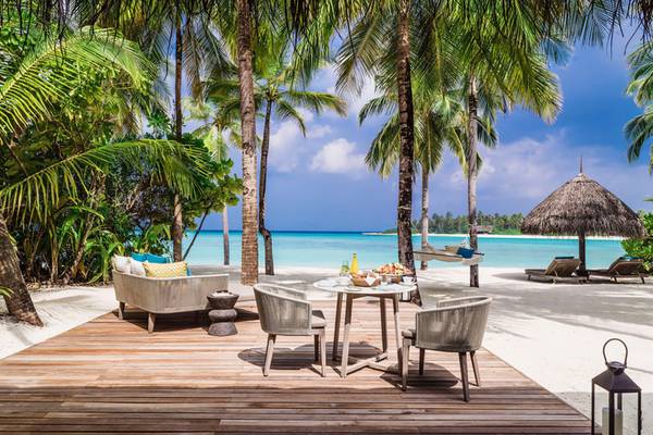 Außensitzecke im One & Only Reethi Rah Hotel mit Blick auf das Meer und Palmen.