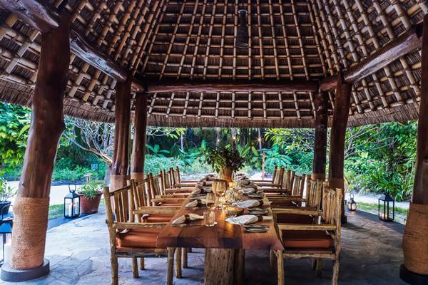 Ein Essbereich im Freien im One & Only Reethi Rah mit einer langen Holztafel und Stühlen.