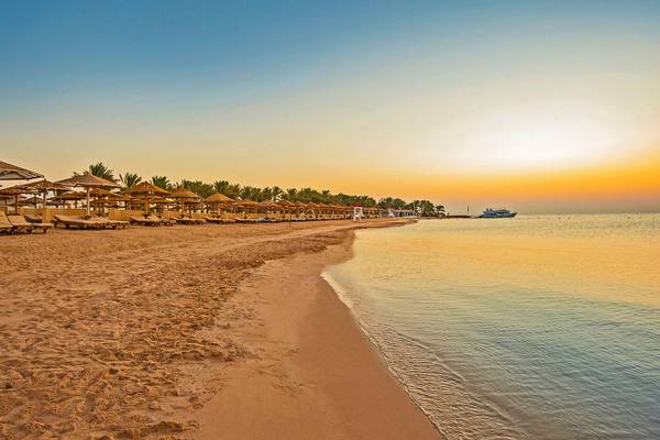 Sonnenuntergang am Strand des SUNRISE Royal Makadi Resort mit leeren Sonnenliegen und einem Boot im Wasser.