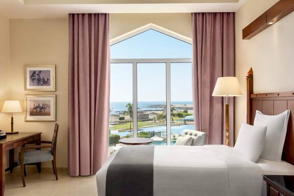 Zimmer im Wyndham Garden Salalah Mirbat Hotel mit Meerblick, großes Bett, Schreibtisch und Panoramafenster.