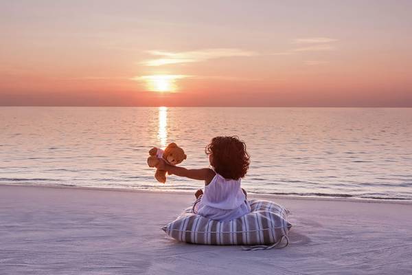 Ein kleines Mädchen sitzt am Strand und beobachtet den Sonnenuntergang.
