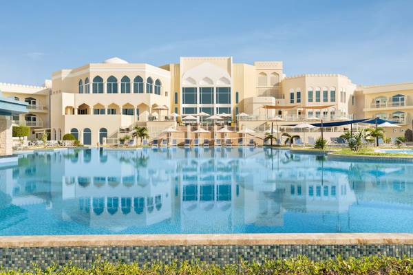Außenbereich des Wyndham Garden Salalah Mirbat Hotels mit großem Pool und Sonnenschirmen.