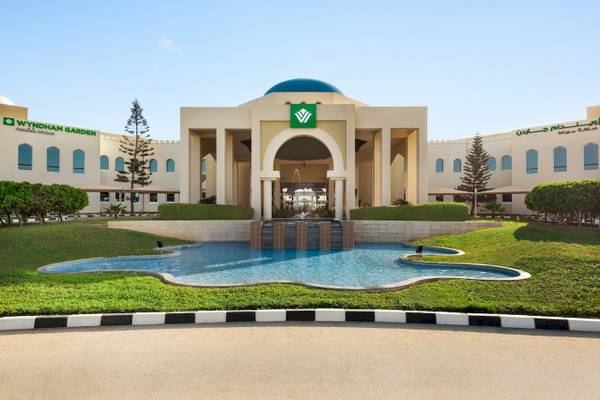 Außenansicht des Wyndham Garden Salalah Mirbat Hotels mit Brunnen und Rasenfläche.