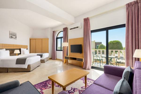 Wyndham Garden Salalah Mirbat Hotelzimmer mit zwei Betten, Fernseher, Tisch und Sofas.