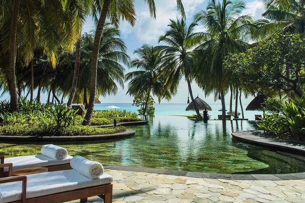 Außenpool mit Liegen und Palmen im One & Only Reethi Rah Hotel.