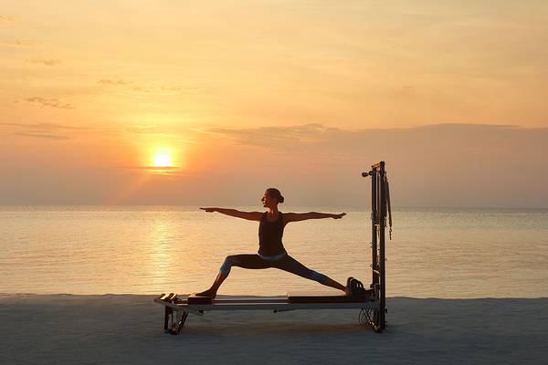 Eine Frau praktiziert Yoga auf einer Pilates-Reformer-Maschine am Strand bei Sonnenuntergang.