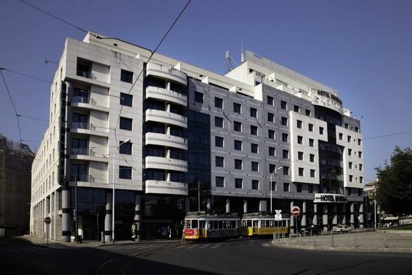 Ein großes weißes Hotel namens Mundial Hotel vor einer Straße mit einer gelben und roten Straßenbahn.