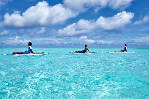 Drei Personen machen Yoga auf Surfbrettern im kristallklaren Wasser des RIU Atoll Hotels.