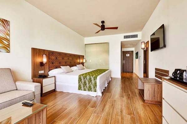 Innenansicht des Riu Atoll Hotelzimmers mit Bett, Fernseher und Holzboden.