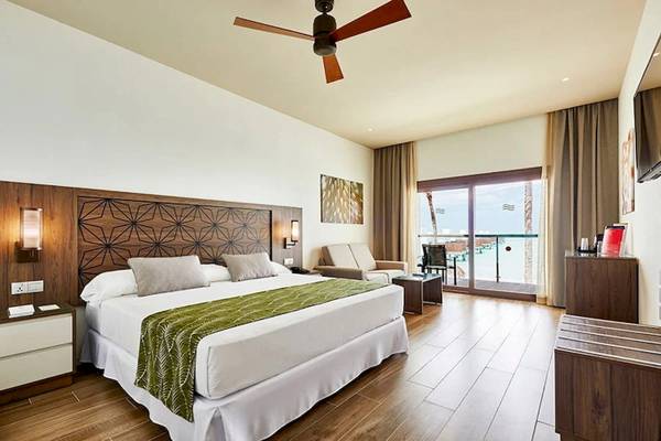 Innenansicht des Schlafzimmers im RIU Atoll Hotel mit Bett, Sofa, Fernseher und Terrassentür.