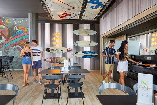 Gäste im RIU Atoll Hotel in der Bar mit bunten Wandmalereien und Surfbrettern.