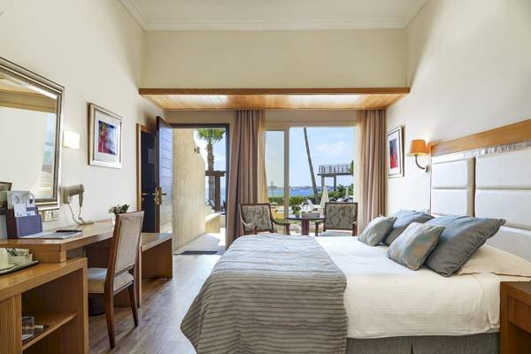 Innenansicht eines Hotelzimmers im Alexander The Great Hotel mit einem Bett, Schreibtisch und Aussicht auf das Meer.