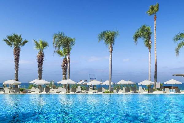 Alexander The Great Hotel Pool mit Sonnenschirmen und Palmen am Meer