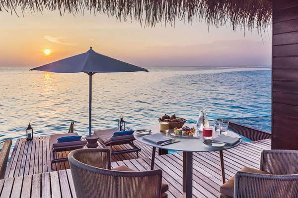 Sonnenuntergang auf der Terrasse des One & Only Reethi Rah Hotels mit einem Tisch und einem Schirm.