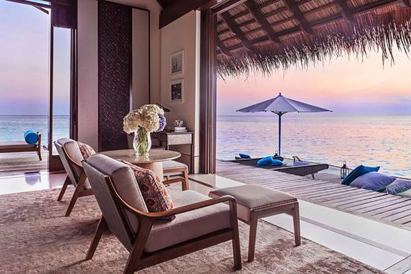 Hotel Suite des One & Only Reethi Rah mit Blick auf das Meer und eine Terrasse mit Möbeln und einem Sonnenschirm.