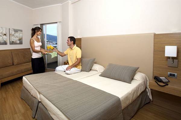 Eine Frau überreicht einem Mann im Be Live Adults Only Tenerife Hotel ein Tablett mit Getränken in einem luxuriösen Zimmer.