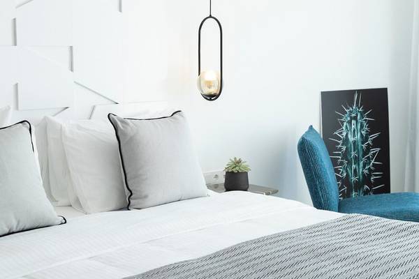 Modernes Schlafzimmer mit weißem Bett, grauer Kissen, blauer Stuhls und Pendeleuchte