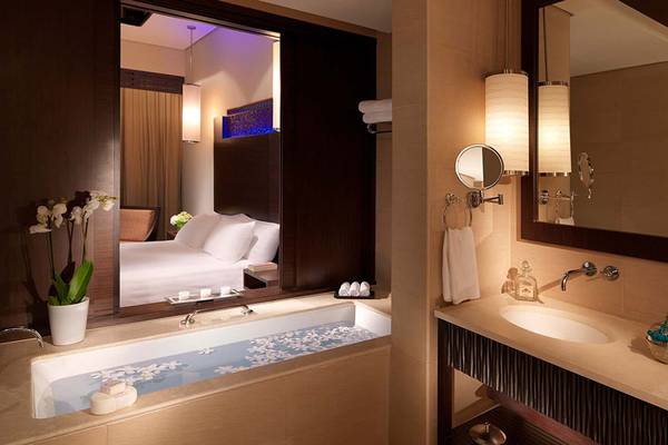 Badezimmer im Anantara The Palm Dubai Resort mit Badewanne, Spiegel und Doppelbett im Hintergrund.