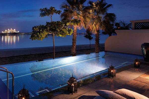 Nachtansicht des Swimmingpools im Anantara The Palm Dubai Resort mit Blick auf die Skyline und Palmen.