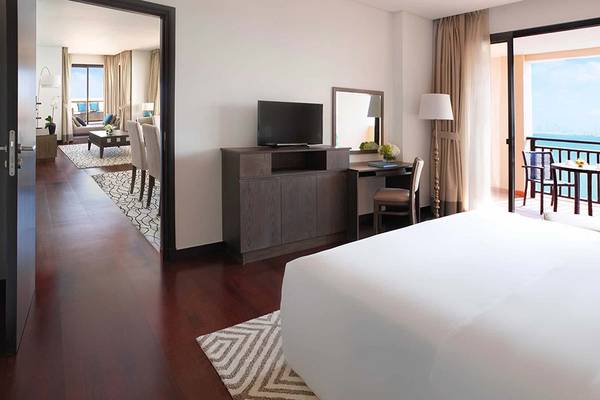 Innenansicht eines Hotelzimmers im Anantara The Palm Dubai Resort mit einem großen Bett, einem Schreibtisch, einem Fernseher und einer Terrasse mit Meerblick.