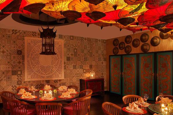 Inneneinrichtung des Anantara The Palm Dubai Resort mit rotem und gelbem Sonnenschirmen an der Decke, gemusterten Wänden und Tisch mit Kerzen.
