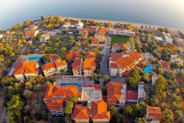 Luftaufnahme des Kampos Village Resorts mit mehreren Gebäuden, roten Dächern und Swimmingpools vor einer Küstenlinie.