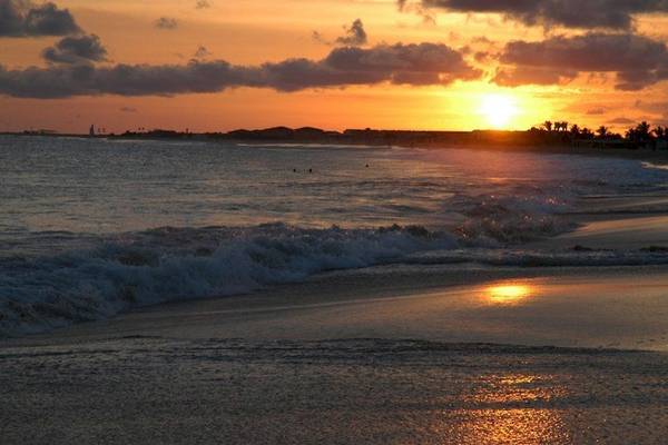 Sonnenuntergang am Strand mit Wellen, die auf den Strand treffen.