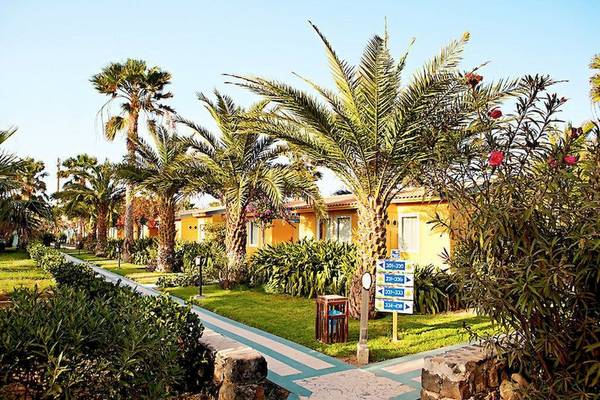 Gelbe Gebäude des VOI Vila Do Farol Resorts umgeben von Palmen und Pflanzen.