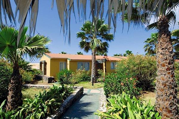 Außenansicht des VOI Vila Do Farol Resorts mit gelbem Gebäude, roten Dach, umgeben von Palmen und Pflanzen
