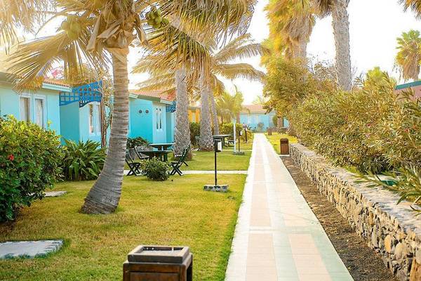 Außenbereich des VOI Vila Do Farol Resorts mit bunten Gebäuden, Palmen und einem gepflasterten Weg.