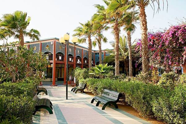 Eingangsbereich des VOI Vila Do Farol Resorts mit grünen Bänken und Palmen.